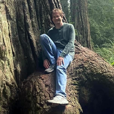 Joe sitting on a root of a redwood tree.